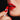 Glossy blood-red lips against a dark background, a hand applying red lipstick