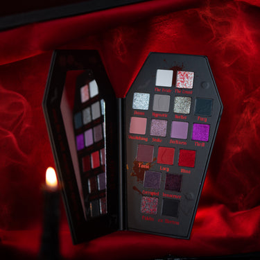 Open Dracula X Jolie Beauty 17-shade eyeshadow palette on red fabric with crimson smoke and candlelight.